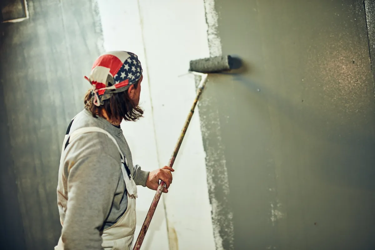 Painter rolling dark gray paint onto an interior wall