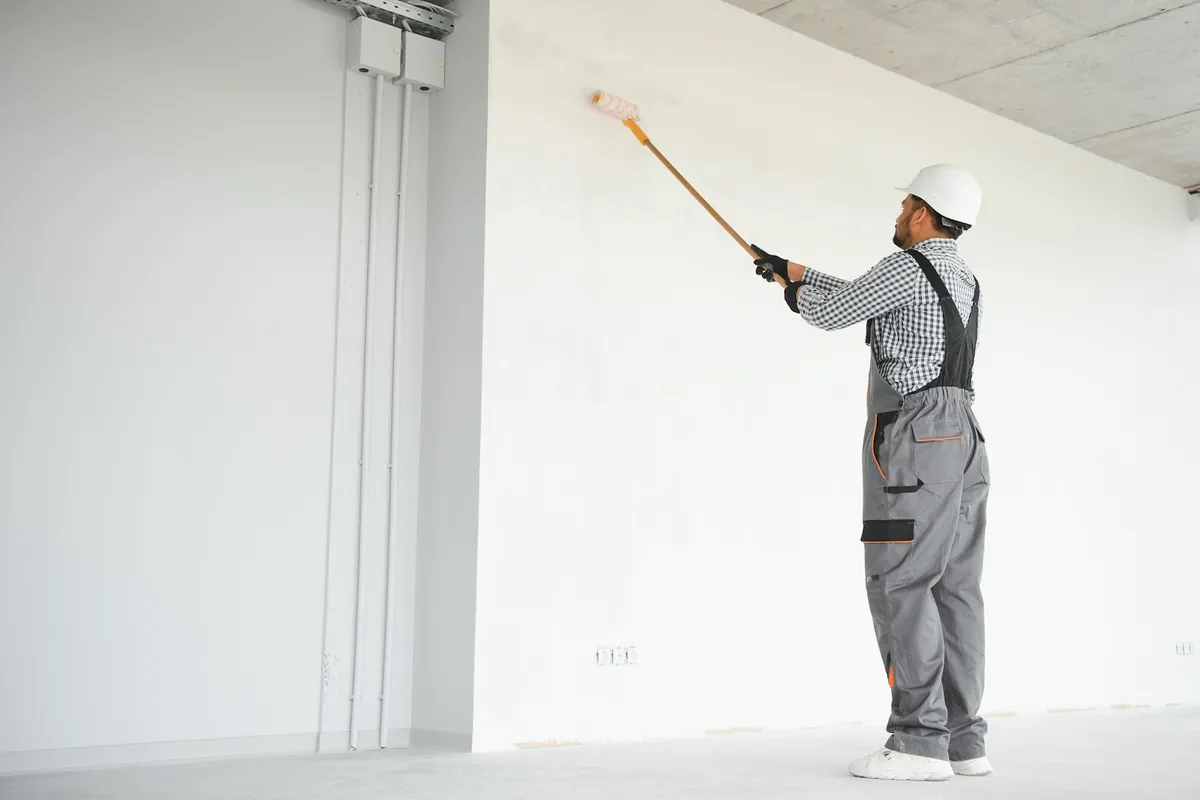 Painter rolling white paint onto a tall commercial wall