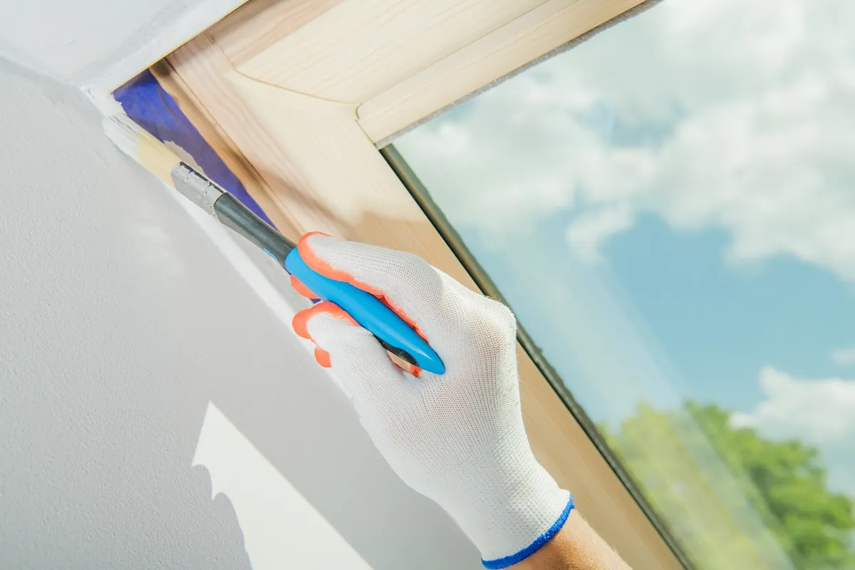 Painter brushing paint along a window frame