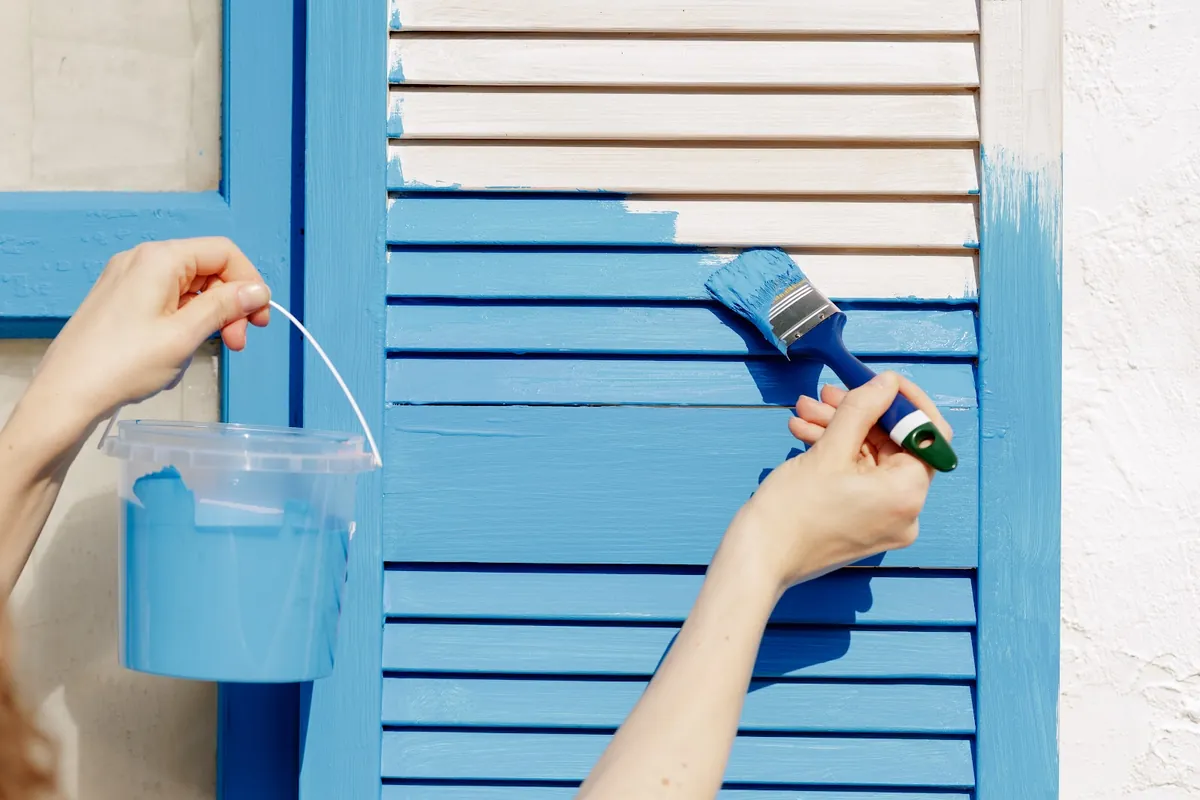 Hands painting wooden window shutters bright blue