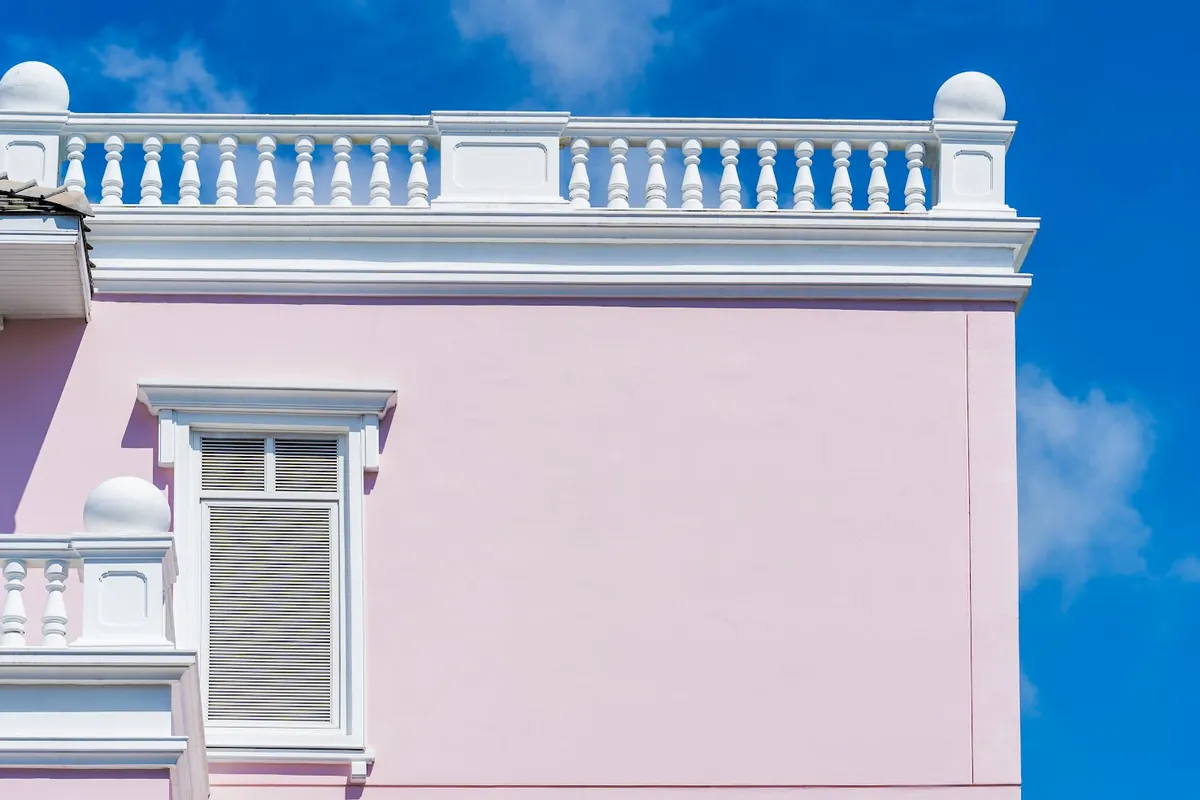 Pink stucco wall with a white balustrade against a blue sky