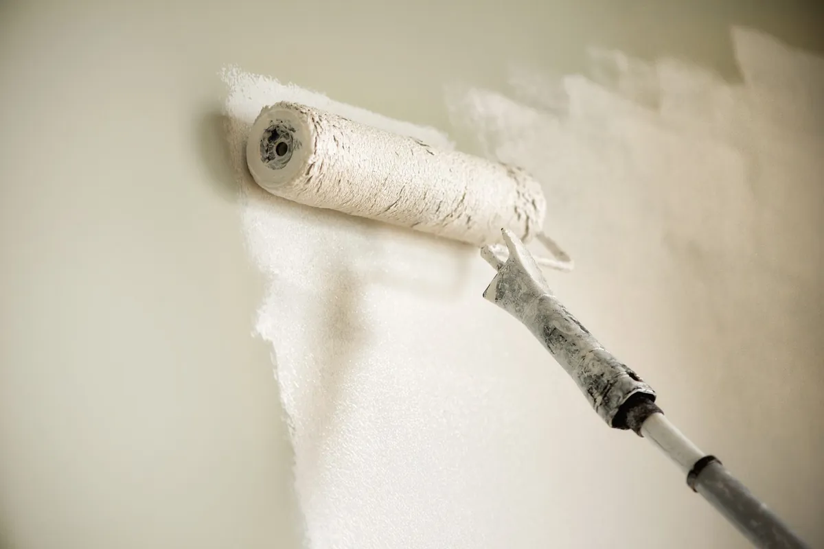 Roller applying cream paint over a white wall