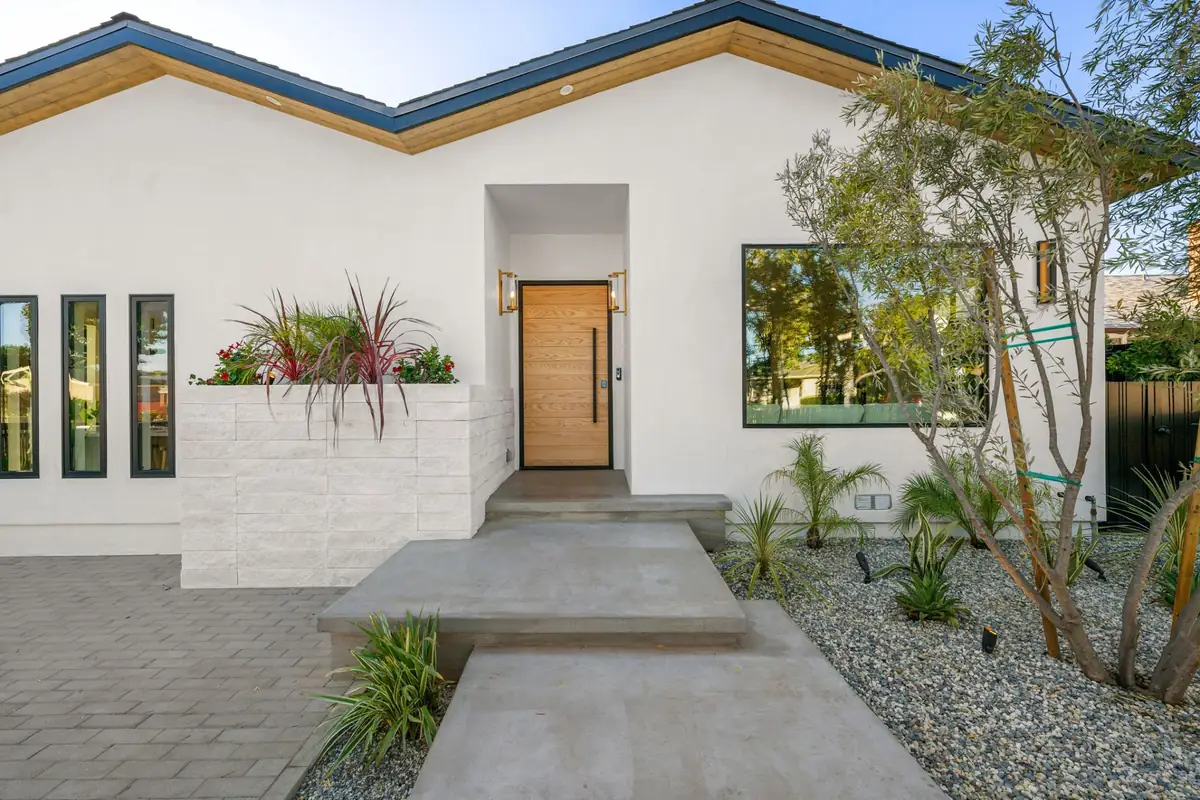 Freshly painted white stucco home with a wood front door, black window frames and a gravel garden